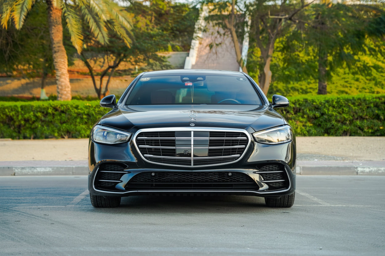 A black Mercedes-Benz S-Class sedan photographed from the front in an outdoor parking area with trees and hedges in the background.